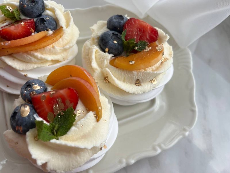 Три міні-павлови з кремом, полуницями, чорницями та персиком на білій тарілці