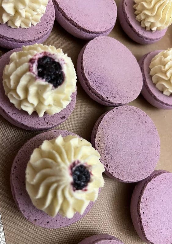 Процес начинення лавандових макаруні — кремова трубочка та свіжа ожина між шкаралупками